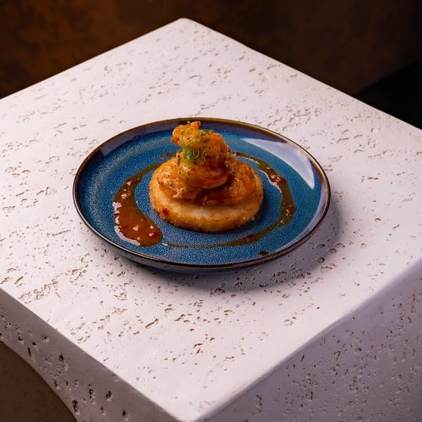 Succulent shrimp in a rich orange sauce with herbs on a crispy fried base, on a blue plate.