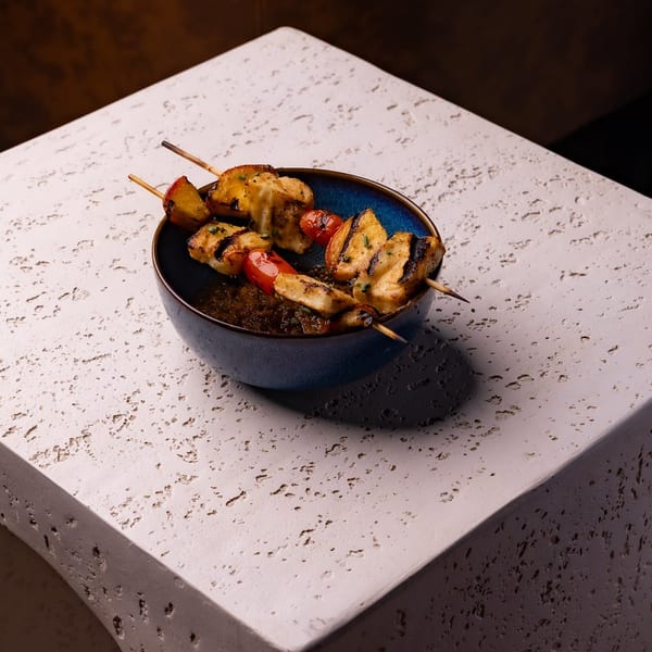 Grilled chicken and vegetable skewers in a blue bowl with sauce on a textured stone surface.