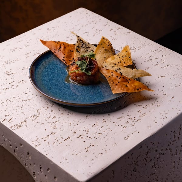 Tartare appetizer with crispy chips and greens on a blue plate, set on a textured stone surface.