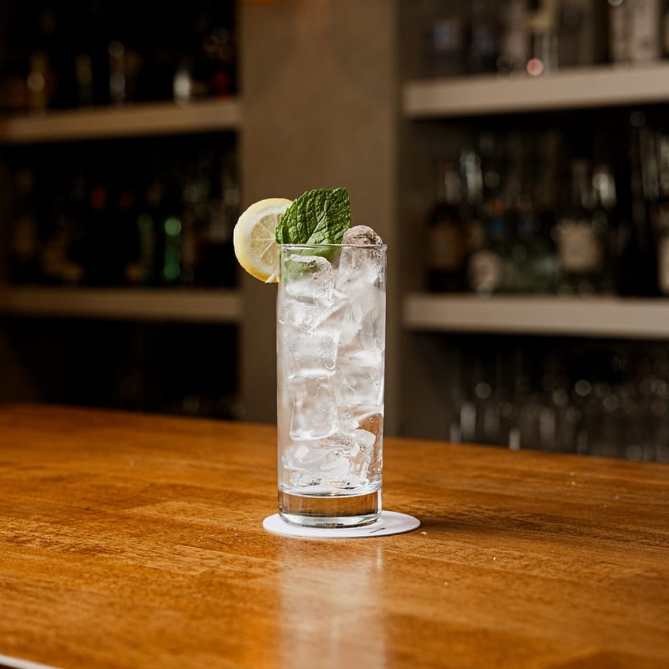 A tall glass with ice, lemon, and mint on a wooden bar counter.