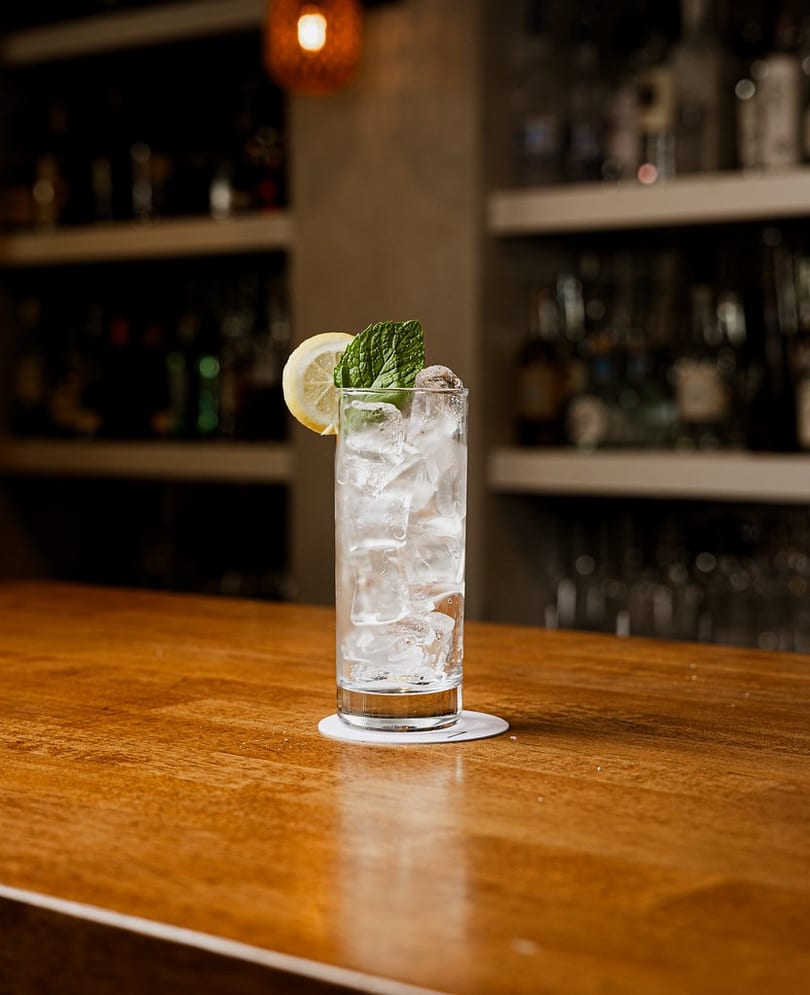 A tall glass with ice, lemon, and mint on a wooden bar counter.