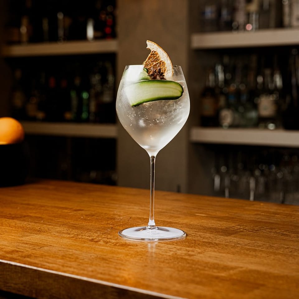 Refreshing cocktail with cucumber and dried orange slice on a polished wooden bar.