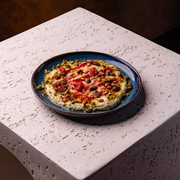 Creamy dessert with red sauce, pistachios, and dried fruit on a blue plate, on a textured block.