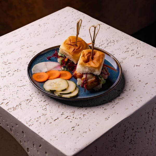 Two sliders with pickled vegetables on a blue plate, resting on a textured white table.